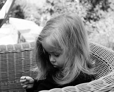 grayscale photo of girl sitting on rattan chair