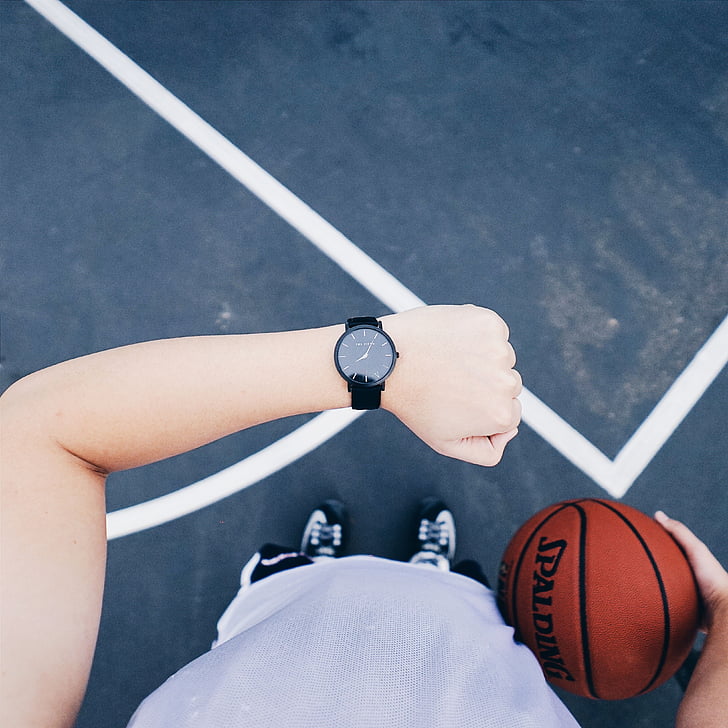 person looking at black analog watch holding Spalding basketball