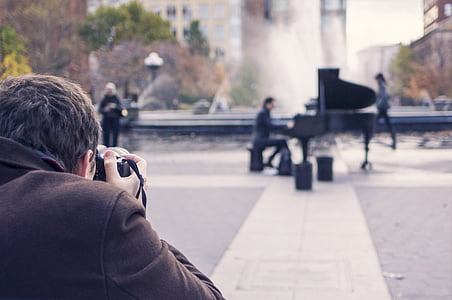 man taking photo of man playing piano near fountain at daytime