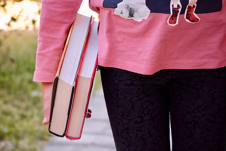 person wearing pink sweatshirt and black bottoms holding two harboard books