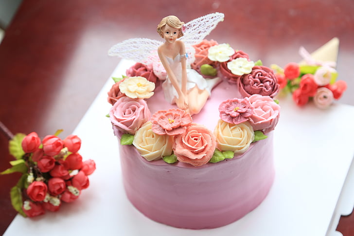 pink icing covered cake on table with fairy figurine