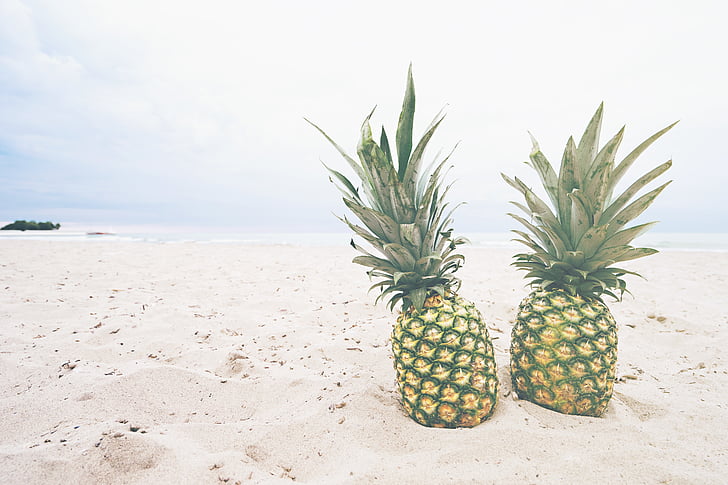 two pineapples on beach sand