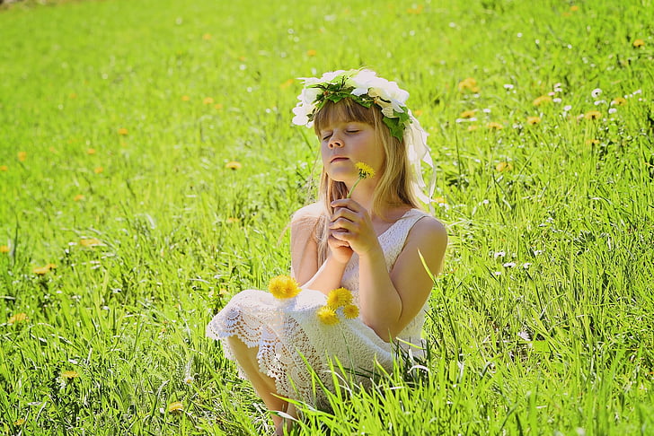 girl wearing floral sleeveless dress with flower crown sitting on green grass field during daytime