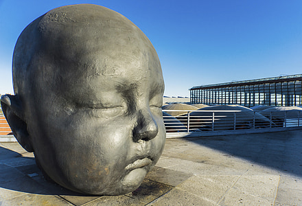 baby's face statue on pavement near handrails at daytime