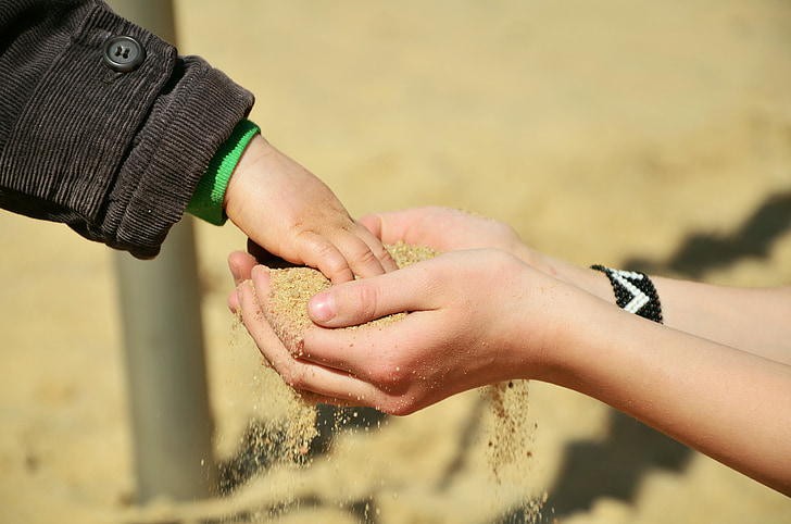 child's hand on other person's hands with sand at daytime