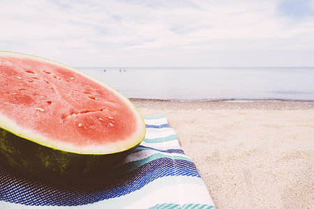 sliced watermelon on blue and white textile near seashore