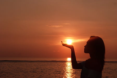 silhouette of woman raising right hand during sunset