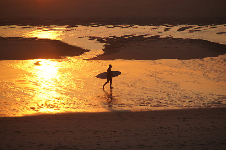man holding surfboard near seashore during dawn