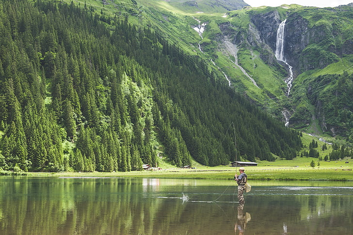 man fishing on lake near green forest