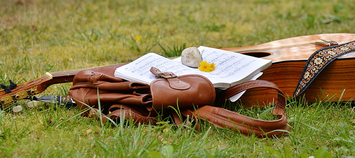 brown acoustic guitar beside brown leather bag on grass field