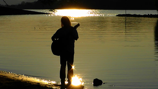 person playing guitar infront of body of water during daytime