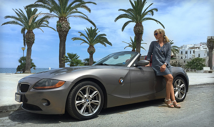 woman in gray long-sleeved dress beside gray BMW convertible coupe during daytime