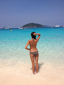 woman standing on seashore overlooking the boat and island during daytime