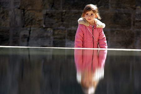 girl wearing white and pink fleece collared topcoat standing near body of water