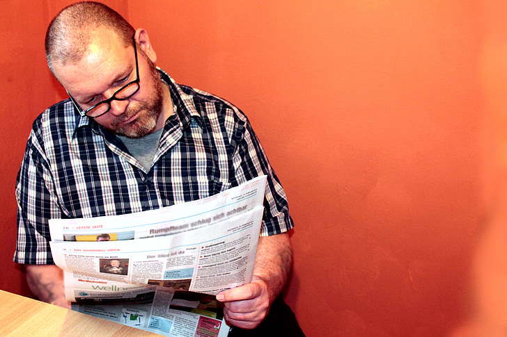 man wearing black and white plaid button-up sport shirt while reading newspaper
