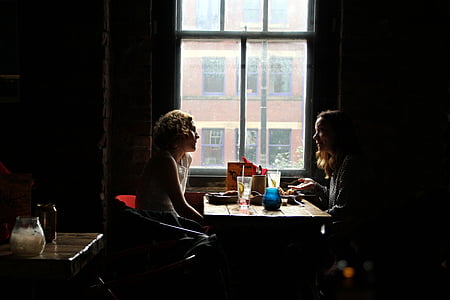 two woman deside table near window