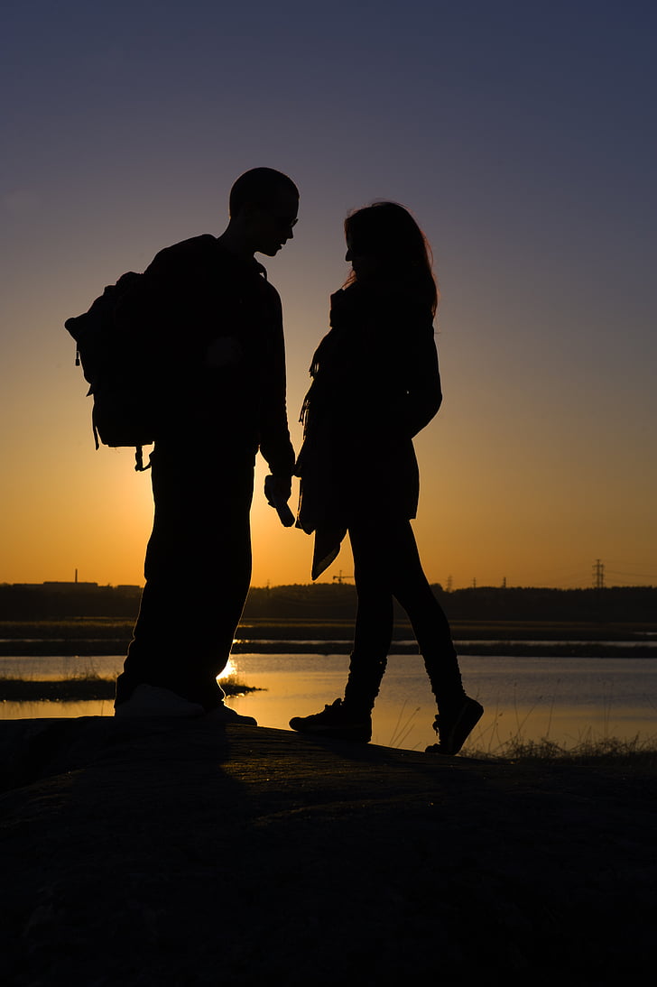 man and woman standing in front of each other near body of water in silhouette photography during golden hour