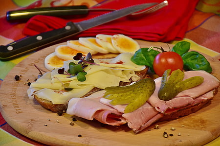 sliced ham, red tomato fruit and sliced fruit on brown wooden chopping board