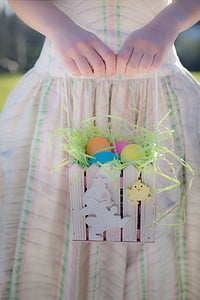 girl in pink and green stripe dress holding basket of easter eggs