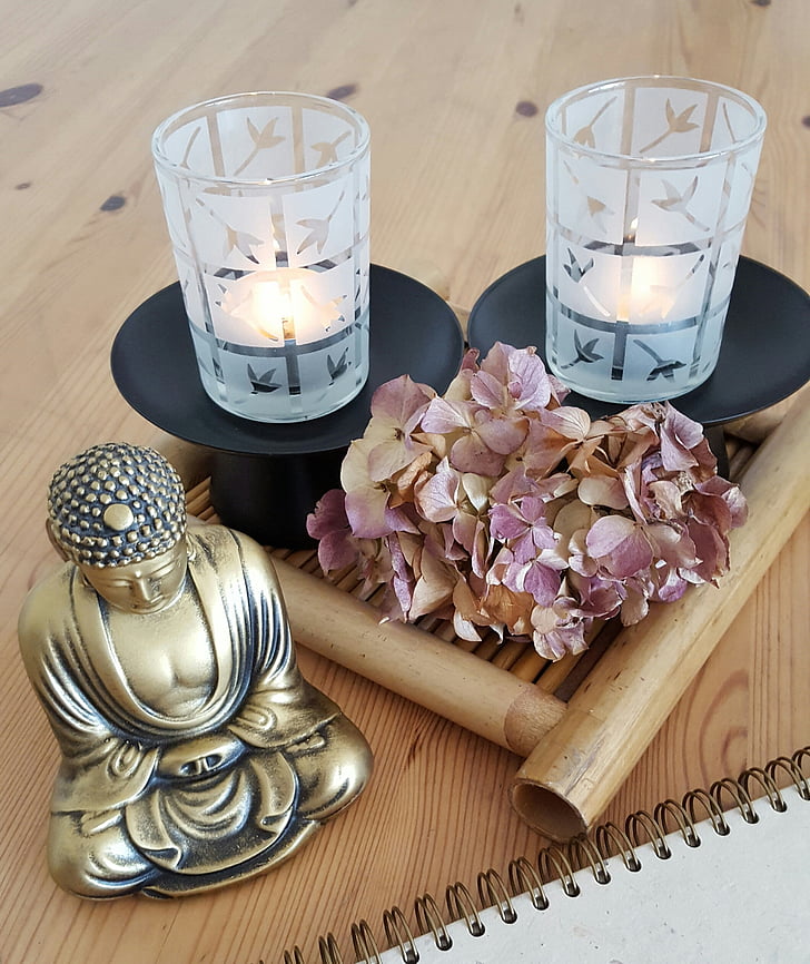 gold-colored Buddha figurine beside purple withered hydrangea flowers and two frosted glass candle holders