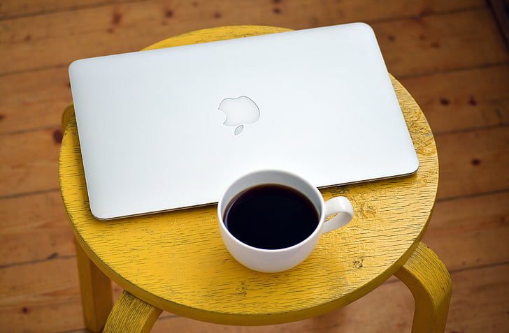 black coffee filled white cup and MacBook Air on top of brown wooden table
