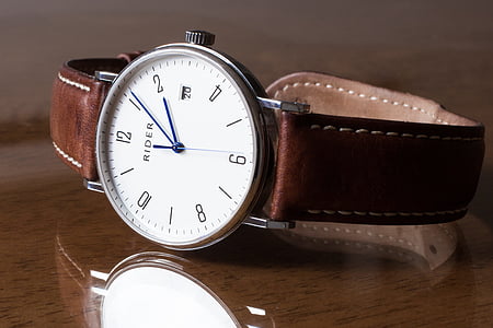 round silver-colored analog watch with brown leather strap on brown wooden surface