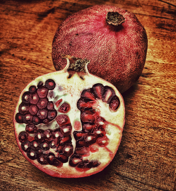 red sliced pomegranate on brown wooden surface