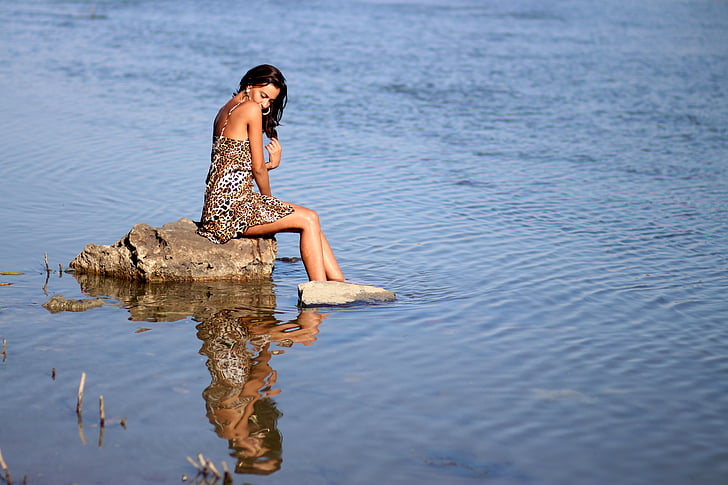 woman sitting on gray rock with feet in water