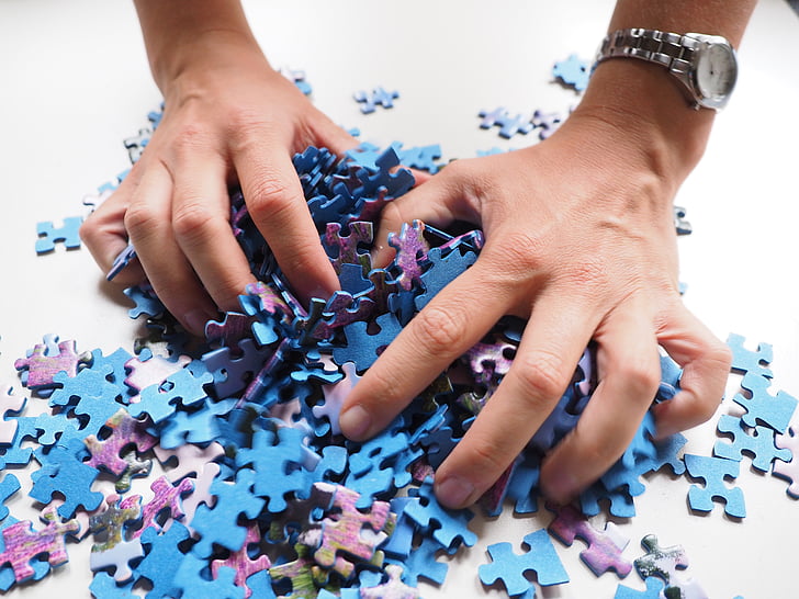 person grabbing bunch of blue and purple jigsaw puzzle pieces