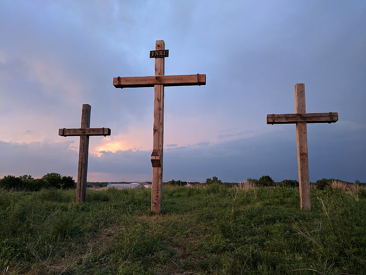 three brown wooden cross on grass hill