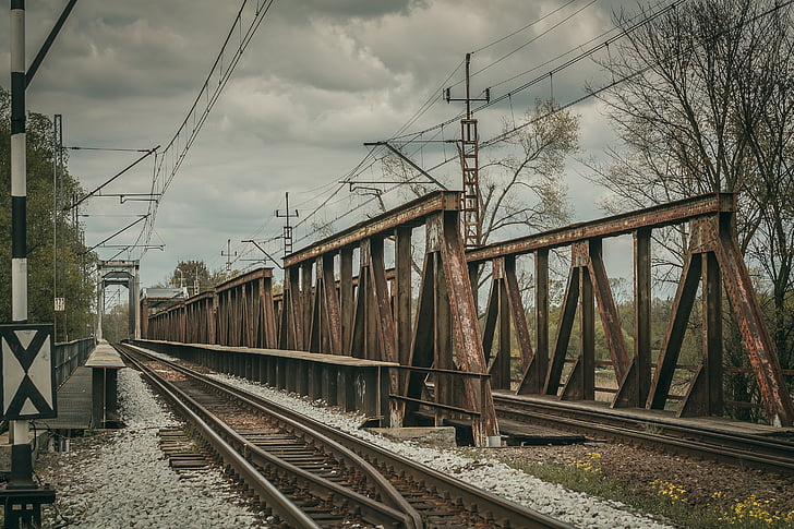 rusted brown metal bridge with train rails under cloudy sky during daytime