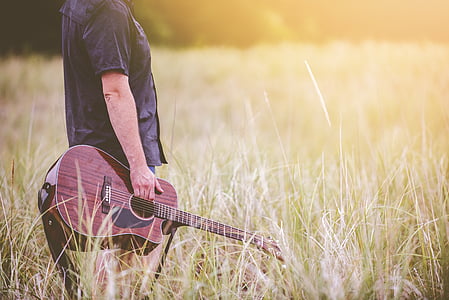 man holdign a acoustic guitar standing on grass