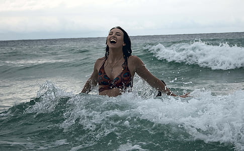 woman wearing black bikini top swimming on body of water while laughing during daytime