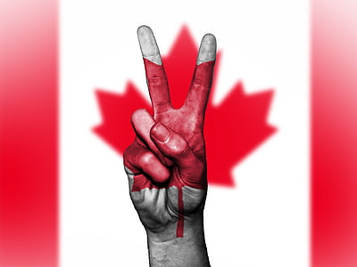 person's right hand forming peace symbol with Canada flag background