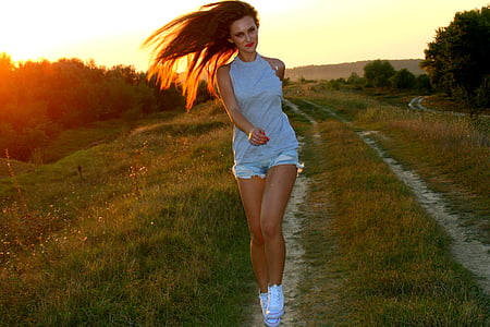 woman wearing white sleeveless top and gray short shorts walking on desired pathway during golden hour