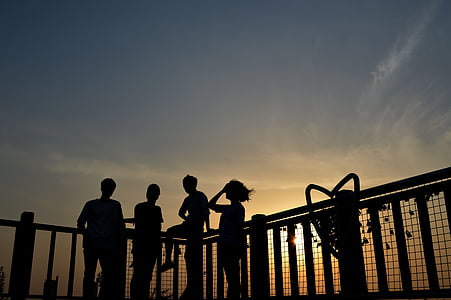 silhouette of four people beside fence during sunset