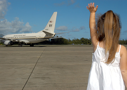girl in white spaghetti strap dress waving at white passenger airplane