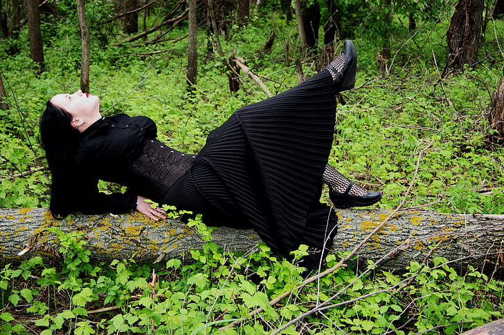 woman in black long-sleeved dress laying on tree trunk