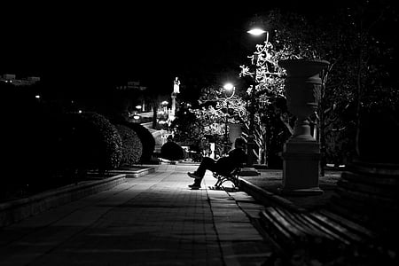 grayscale photo of person sitting on bench near street light