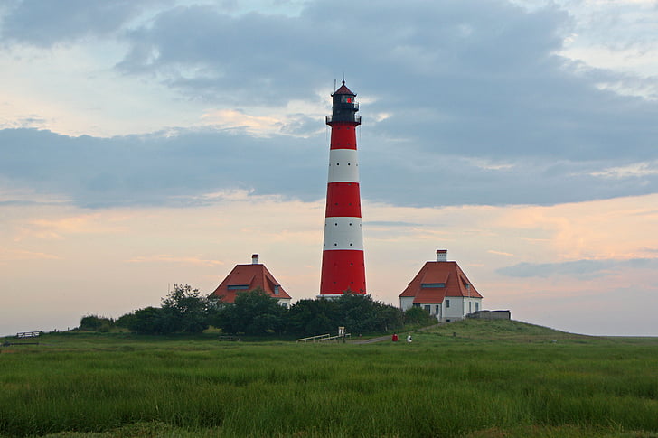 lighthouse between two house under cumulus cloud
