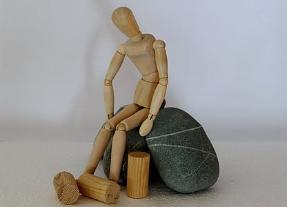 human shaped wooden toy sits on black stones