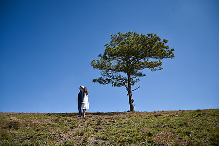 man and woman standing side by side on field near tree