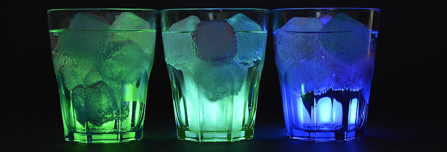 three rocks glasses filled with liquid and ice against black background