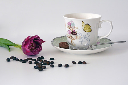 white ceramic teacup and saucer plate with spoon beside purple petaled flower and coffee beans