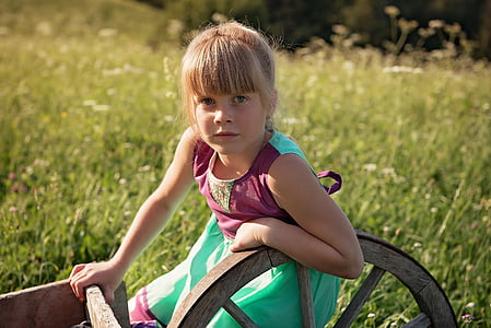 girl in maroon and teal sleeveless dress holding wagon wheel near green grass