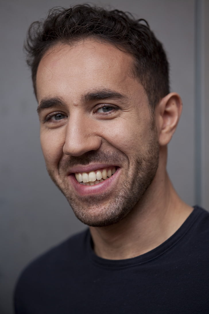 smiling man in black crew neck shirt beside a white wall