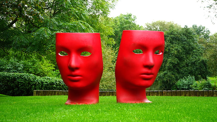 two red mask statue on green grass surrounded by trees