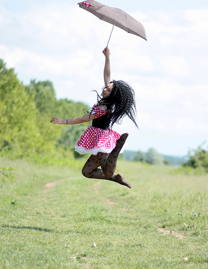 woman holding umbrella jumping on green grass field