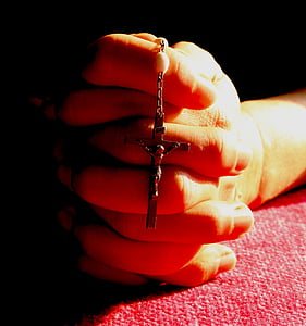 person praying while holding crucifix pendant necklace