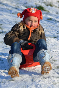 girl wearing brown zip-up jacket blue denim jeans on red sled